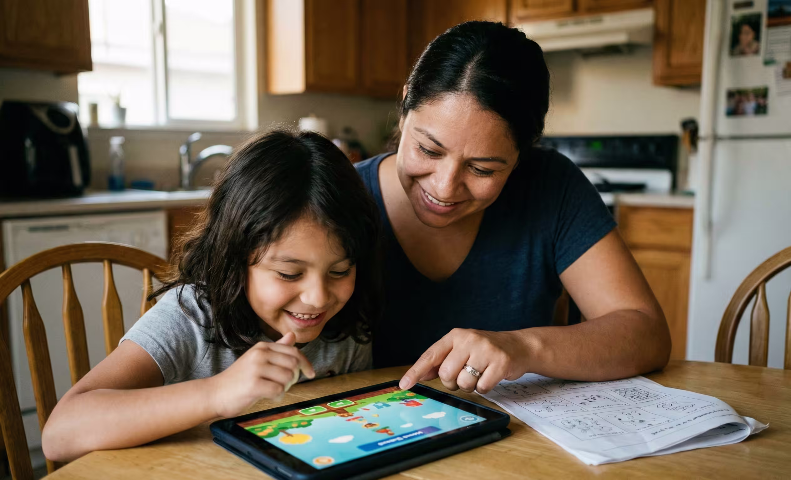 A mother and her neurodiverse child smiling and engaged with a learning app on a tablet at a kitchen table, with a discarded worksheet pushed aside, illustrating alternative learning strategies.