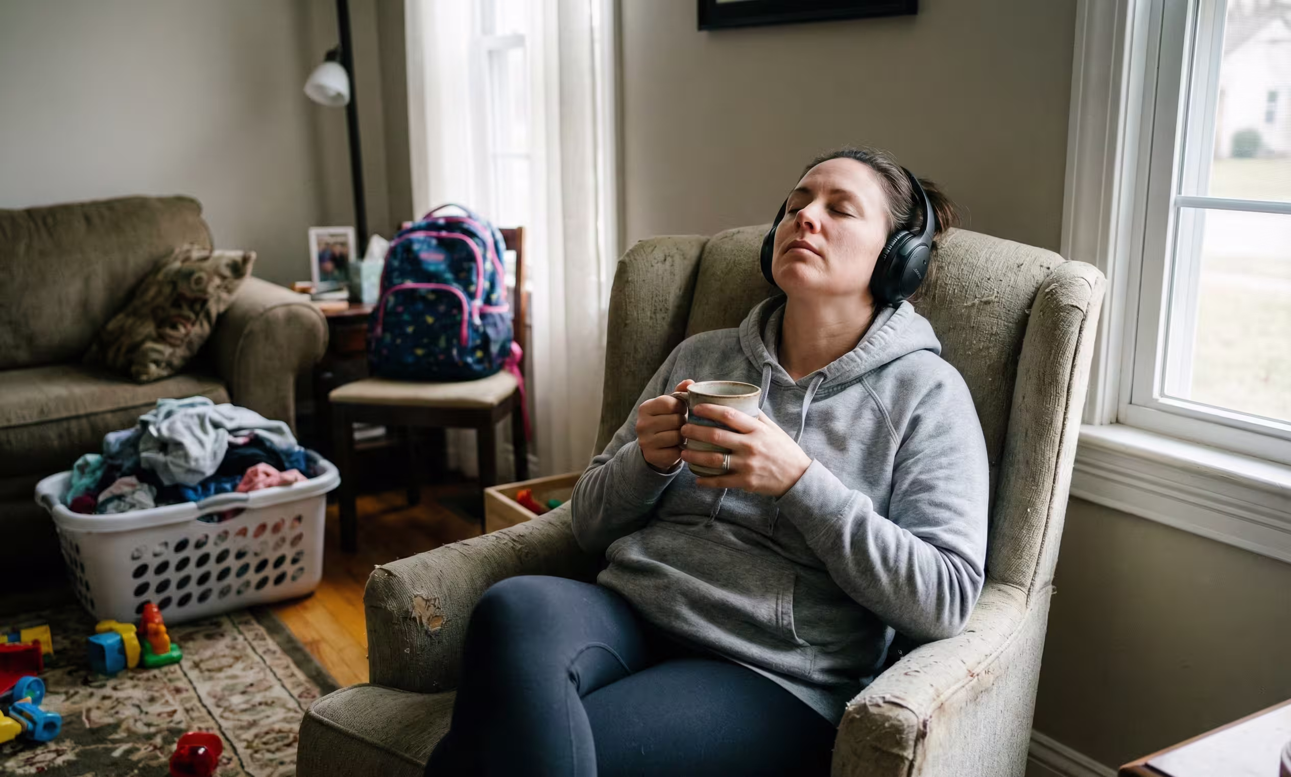 A mother in a real-life living room takes a mindful micro-break with headphones and a mug, illustrating the concept of practical self-care and psychological resilience for parents of disabled children to prevent burnout.